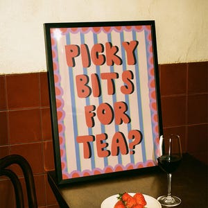 Può includere: Una stampa incorniciata con la scritta "PICKY BITS FOR TEA?" in lettere rosse. La stampa ha uno sfondo a righe con un bordo smerlato. Un piatto di fragole e un bicchiere di vino rosso sono su un tavolo scuro.