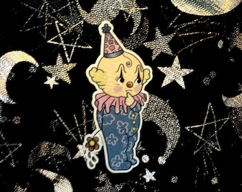 May include: A sticker featuring a cartoon clown with a sad expression. The clown wears a blue outfit with flower and cloud patterns, a pink ruffled collar, and a party hat. The background is black with silver stars and crescent moons.