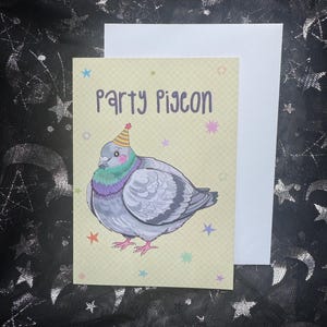 May include: A greeting card with a cartoon pigeon wearing a party hat. The card reads "Party Pigeon" in purple text. The pigeon is gray with a green and purple chest. Colorful stars decorate the background.