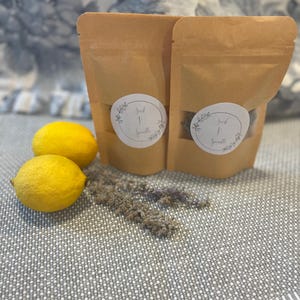 May include: Two brown paper pouches with white labels that read "Seed & Sprout" are displayed next to two yellow lemons and sprigs of lavender. The pouches are sealed and stand upright on a gray and white patterned surface.