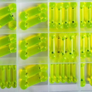 May include: A clear plastic organizer filled with neon green fishing bobbers. The bobbers are cylindrical with a rounded end and a small, clear tube. The organizer has multiple compartments, each holding several bobbers.