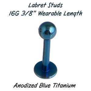 May include: Anodized blue titanium labret stud. The stud has a ball top and a flat disc base. The text on the image reads "Labret Studs 16G 3/8" Wearable Length" and "Anodized Blue Titanium."