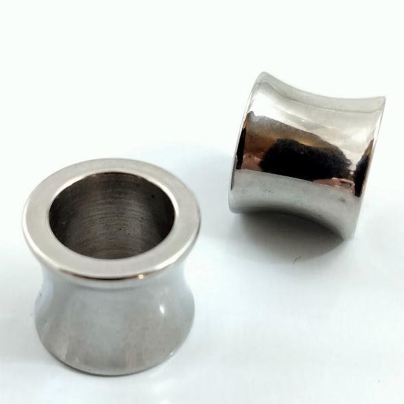 May include: Two polished, silver-colored ear gauges. The gauges have a flared design, with a wider outer rim and a narrower center. The smooth, metallic surface reflects light, creating highlights and shadows. The gauges are designed for stretched earlobes.