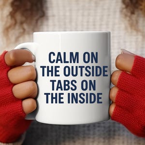 Może przedstawiać: Biały ceramiczny kubek z napisem "CALM ON THE OUTSIDE TABS ON THE INSIDE" w kolorze granatowym. Kubek trzyma osoba w czerwonych rękawiczkach bez palców.