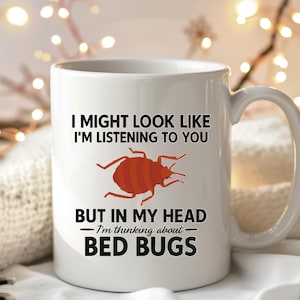 May include: White ceramic mug with the text "I MIGHT LOOK LIKE I'M LISTENING TO YOU BUT IN MY HEAD - I'm thinking about - BED BUGS" and a cartoon bed bug illustration. The mug has a curved handle.