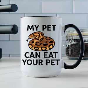 May include: White ceramic mug with a black handle and rim. The mug features the text "MY PET CAN EAT YOUR PET" in black, with a cartoon illustration of a brown and tan snake.