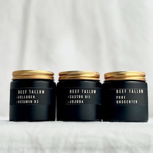 Könnte beinhalten: Drei schwarze Gläser mit goldenen Deckeln werden gezeigt. Jedes Glas hat ein schwarzes Etikett mit weißem Text. Die Etiketten lauten "Beef Tallow" mit verschiedenen Zutatenkombinationen.