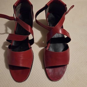 May include: A pair of red sandals featuring an open-toe design, a black insole, and crisscross straps that wrap around the ankle with a silver-toned buckle closure. The text #547 is visible in the upper left corner of the image.