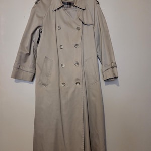 May include: A beige double-breasted trench coat featuring a wide collar, shoulder epaulets, and adjustable sleeve straps. The coat has a button-front closure and a plaid interior lining. The text #362-F is visible in the upper left corner.