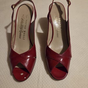 May include: A pair of red patent leather slingback heels with an open toe and a crisscross strap design. The interior insoles feature the text Bruno Magli for Saks Fifth Avenue. The number #545 is visible in the upper left corner of the image.
