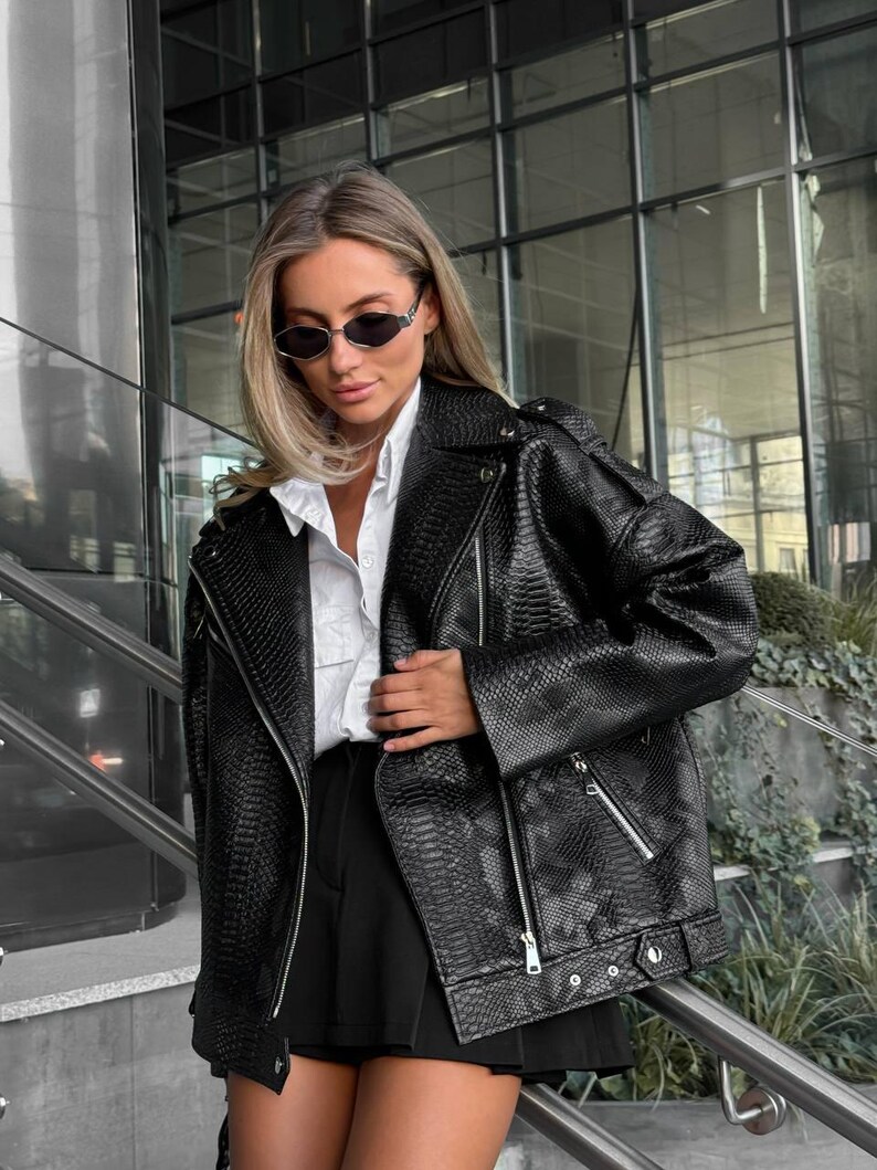 Peut inclure: Veste de motard noire en similicuir avec un motif peau de serpent, fermeture &eacute;clair asym&eacute;trique, plusieurs poches et d&eacute;tails argent&eacute;s. Port&eacute;e sur une chemise blanche et un short noir, l'ensemble d&eacute;gage une allure moderne et tendance.