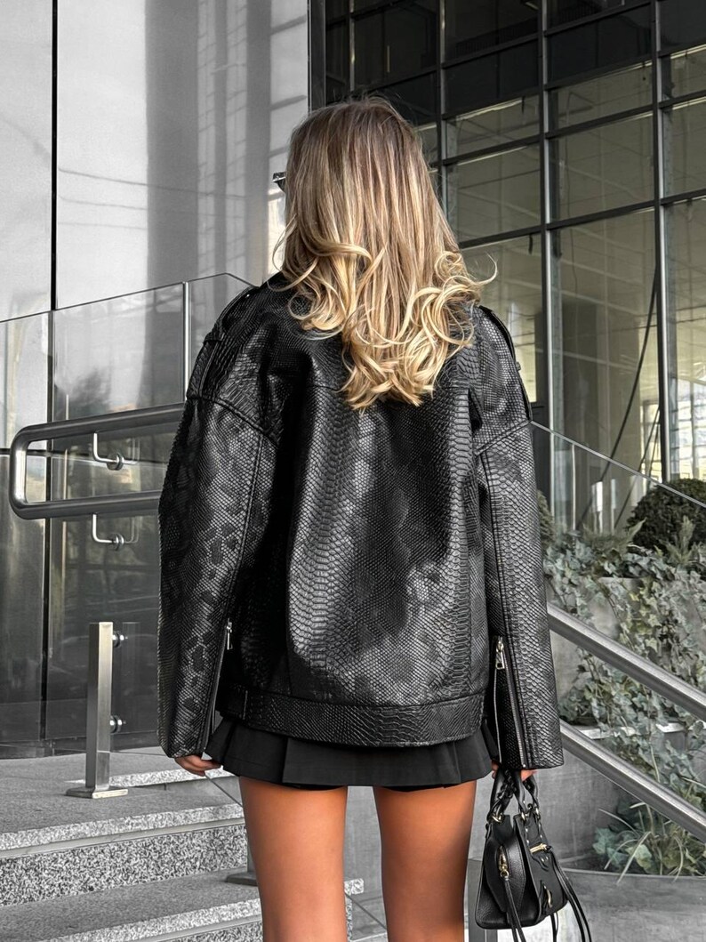 Peut inclure: Veste noire en similicuir avec une texture peau de serpent, fermeture &eacute;clair et petit sac &agrave; main noir. La veste a un style motard classique avec une coupe courte et carr&eacute;e. La mod&egrave;le porte une jupe noire.