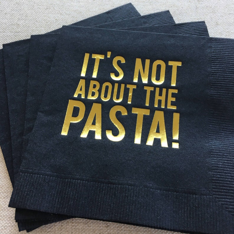 May include: Black paper napkins with gold foil lettering that reads "It's not about the pasta!"