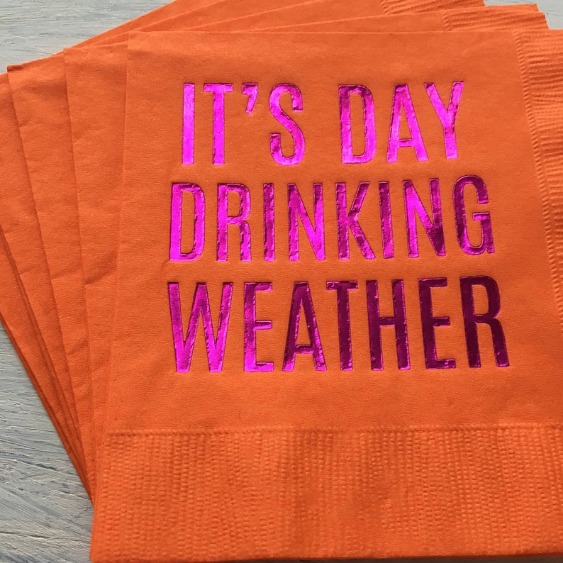 May include: A stack of orange napkins with the text "It's Day Drinking Weather" printed in pink.