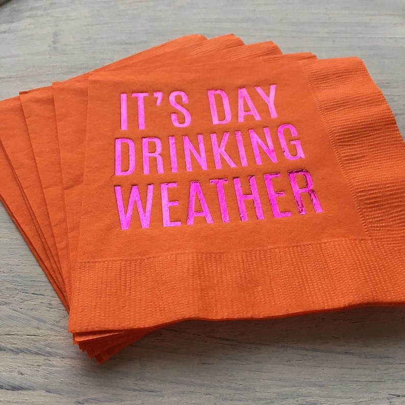 May include: A stack of orange paper napkins with the text "It's Day Drinking Weather" printed in pink.