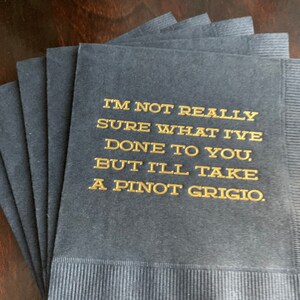 May include: A stack of navy blue cocktail napkins with gold lettering. The text reads, "I'M NOT REALLY SURE WHAT I'VE DONE TO YOU, BUT I'LL TAKE A PINOT GRIGIO."