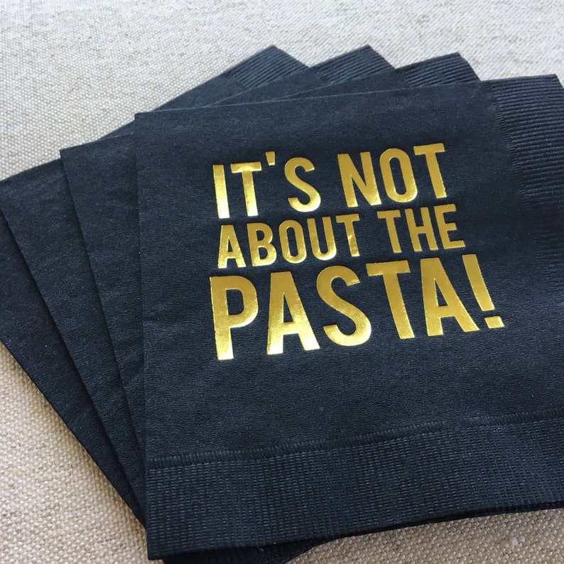 May include: A stack of black paper napkins with gold foil lettering that reads "It's not about the pasta!"