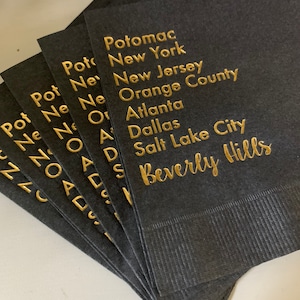 May include: A stack of black napkins with gold foil lettering. The text reads "Potomac, New York, New Jersey, Orange County, Atlanta, Dallas, Salt Lake City, Beverly Hills".