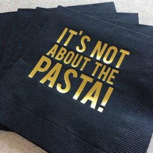 May include: Black paper napkins with gold foil lettering that reads "It's not about the pasta!"
