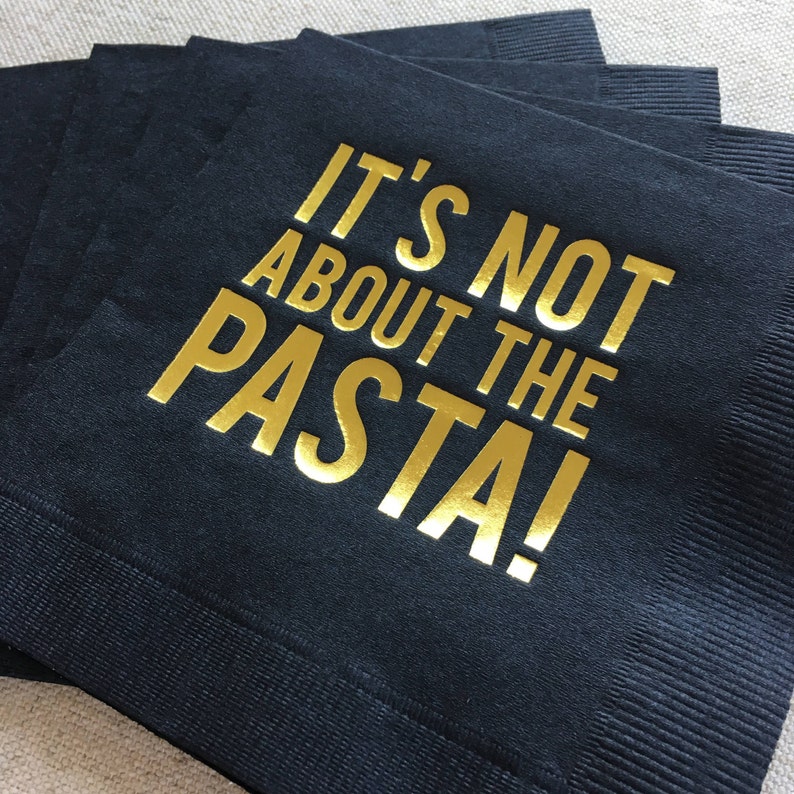 May include: Black paper napkins with gold foil lettering that reads "It's not about the pasta!"