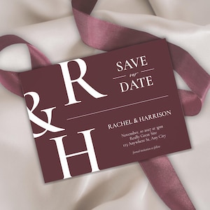 May include: A burgundy Save the Date card with white text and a burgundy ribbon. The card features the text "SAVE our DATE" and the names "RACHEL & HARRISON" along with the date, time, and location of the event.