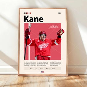 Op de afbeelding: Een verticale poster met een ijshockeyspeler in een rood shirt met een gevleugeld wiel-logo, die een hockeystick vasthoudt en een helm draagt. De tekst luidt Kane, #88, en bevat een biografie en carrièrestatistieken. De achtergrond is crème en rood.