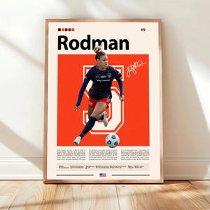 May include: A framed poster featuring a soccer player in action. The poster has a red background with the player's name, "Rodman," in large black letters. The player is wearing a navy blue and red uniform and is kicking a soccer ball.