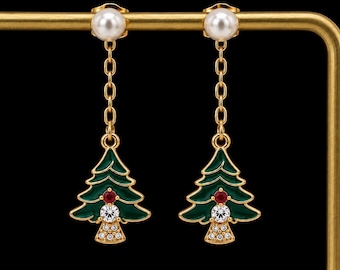 May include: A pair of gold-tone drop earrings featuring a white pearl stud at the top, connected by a short chain to a green enameled Christmas tree charm. The tree is decorated with a small red stone, a clear crystal, and tiny clear stones.