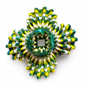 May include: A vibrant, abstract decorative object with a central square element. The design features radiating, layered elements in yellow, green, and white. The central square is a glossy teal color, creating a striking contrast.