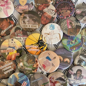 Peut inclure: Une collection de badges ronds avec divers motifs et textes. Certains badges présentent des images de personnes, d'animaux et d'illustrations. Le texte comprend des phrases telles que "You're Not Diversified" et "Closing the Distance."