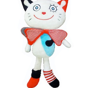 May include: A soft toy cat with a white body, a red and white striped bow tie, and red and black details. The cat has a smiling face with blue eyes and a red heart nose. The doll's feet are red and black.