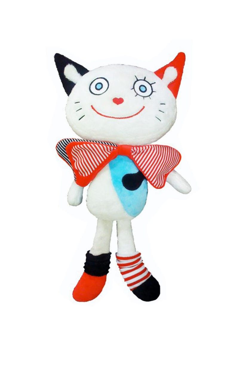 May include: A soft toy cat with a white body, a red and white striped bow tie, and red and black details. The cat has a smiling face with blue eyes and a red heart nose. The doll's feet are red and black.