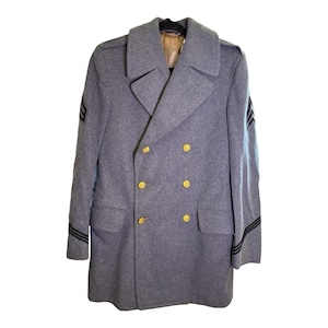 May include: A grey double-breasted wool coat featuring wide lapels, six gold-toned buttons, and two flap pockets. Each sleeve displays three black horizontal stripes, and the interior collar area is lined with a tan fabric material.