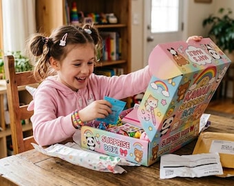 May include: A colorful cardboard surprise box featuring cartoon panda and bear illustrations, rainbows, and the text Kawaii Surprise Box. The open box contains various small items, with a blue packet being held, alongside a tan shipping envelope.