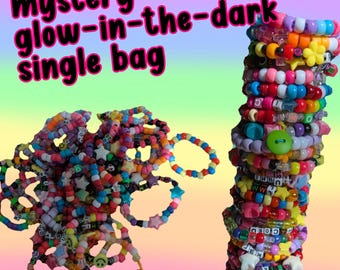 Puede incluir: Una colección de pulseras de cuentas coloridas y una pila de pulseras. Las pulseras están hechas con cuentas de varios colores y formas, incluyendo estrellas y caras sonrientes. El texto "mystery glow-in-the-dark single bag" se muestra en la parte superior de la imagen.