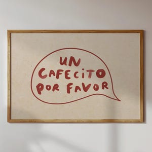 May include: A rectangular wooden frame containing a light beige print with a hand-drawn red speech bubble. Inside the bubble, the text reads UN CAFECITO POR FAVOR in a bold, informal, red, hand-lettered font style on a textured paper background.