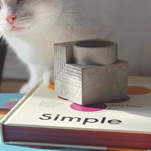 May include: A set of three ceramic mugs with a speckled, matte finish. The mugs are in cream, light grey, and dark grey. Each mug has a simple, minimalist design, ideal for coffee or tea.