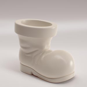 May include: A cream-coloured ceramic boot-shaped planter. The boot features a rounded toe, a short heel, and a wide opening at the top. The surface is smooth and glossy, with subtle details suggesting folds and creases.