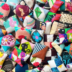 May include: A collection of colorful, handmade star-shaped pillows with various patterns and designs. The pillows feature images of strawberries, butterflies, rainbows, and other whimsical motifs. The fabrics are a mix of textures and colors, creating a vibrant and eclectic display.