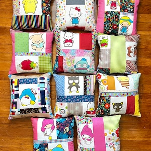 May include: A collection of 12 colorful patchwork pillow covers featuring various cartoon characters, including Hello Kitty, a penguin, and a frog. The pillows are made of different fabrics and have a variety of patterns.