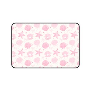 May include: A rectangular mousepad with a repeating pattern of pink seashells, starfish, and bows on a cream background. The design includes heart details within the shells. The mousepad has a black border.