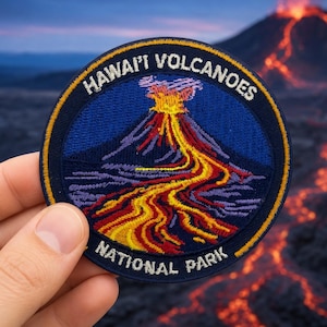 May include: A circular embroidered patch featuring a dark blue background with a central graphic of a volcanic eruption. The design displays a mountain with flowing orange and yellow lava, surrounded by white text reading HAWAI'I VOLCANOES NATIONAL PARK.