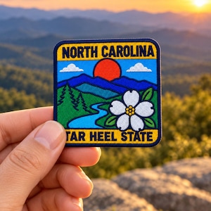 Puede incluir: Un parche bordado cuadrado que muestra un paisaje con un río azul, pinos verdes, montañas azules, un sol rojo y una flor de cornejo blanca. El texto NORTH CAROLINA y TAR HEEL STATE aparece en letras amarillas en la parte superior e inferior.