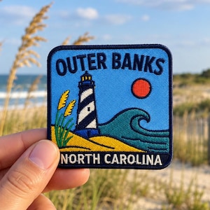 Puede incluir: Un parche bordado cuadrado que muestra un cielo azul, un sol rojo, una ola oceánica verde azulado y un faro a rayas blancas y negras. El texto dice OUTER BANKS en la parte superior y NORTH CAROLINA en la parte inferior, con hierba de playa amarilla.