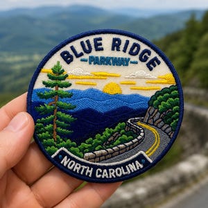 May include: A circular embroidered patch featuring a landscape of the Blue Ridge Parkway in North Carolina. The design includes a tall green pine tree, blue mountain ranges, a yellow sun, and a winding road with a stone wall, bordered by dark blue.