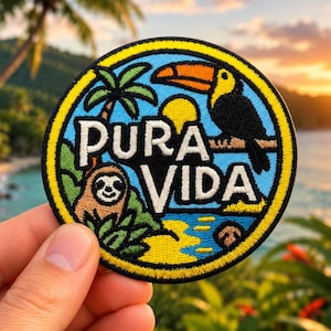 May include: A circular embroidered patch with a black border featuring the text PURA VIDA in white. The design includes a toucan, a sloth, a palm tree, a yellow sun, and a blue ocean scene with a sandy beach, all rendered in vibrant colors.