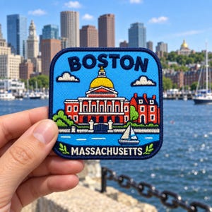 Könnte beinhalten: Ein quadratischer gestickter Aufnäher mit hellblauem Hintergrund, der oben den Schriftzug BOSTON und unten MASSACHUSETTS trägt. Das Motiv zeigt ein rotes Gebäude mit gelber Kuppel, grüne Bäume und ein kleines weißes Segelboot auf blauem Wasser.