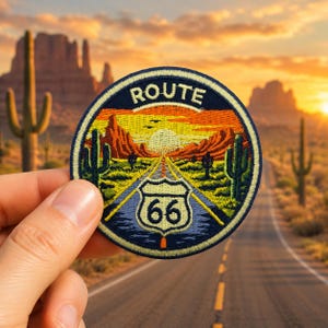 Op de afbeelding: Een ronde Route 66-patch met een woestijnlandschapontwerp. De patch toont een weg die leidt naar een zonsondergang, cactussen en het nummer 66 in een schild. De rand is marineblauw met het woord "ROUTE" in wit.
