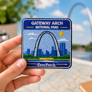 May include: A square patch with a blue border features the Gateway Arch National Park. The patch shows the arch, a blue skyline, a yellow sun, and the text "Gateway Arch National Park" and "EverPatch". The patch is held by a hand.