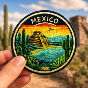 May include: Embroidered patch featuring a vibrant landscape of Mexico. The design includes a pyramid, cacti, and a colorful sunset. The word "MEXICO" is arched across the top in white letters against a navy blue background. The patch is round with a gold border.